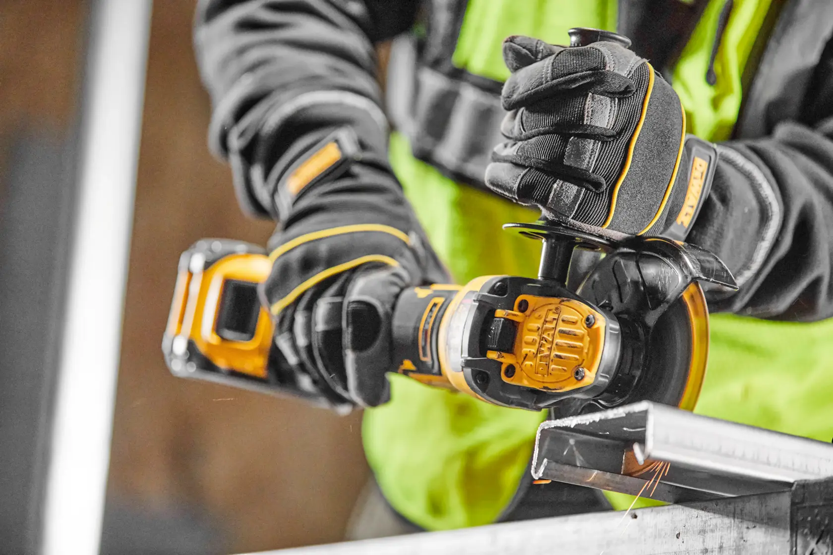 Person using DEWALT cordless grinder with gloves to cut metal on a workbench.