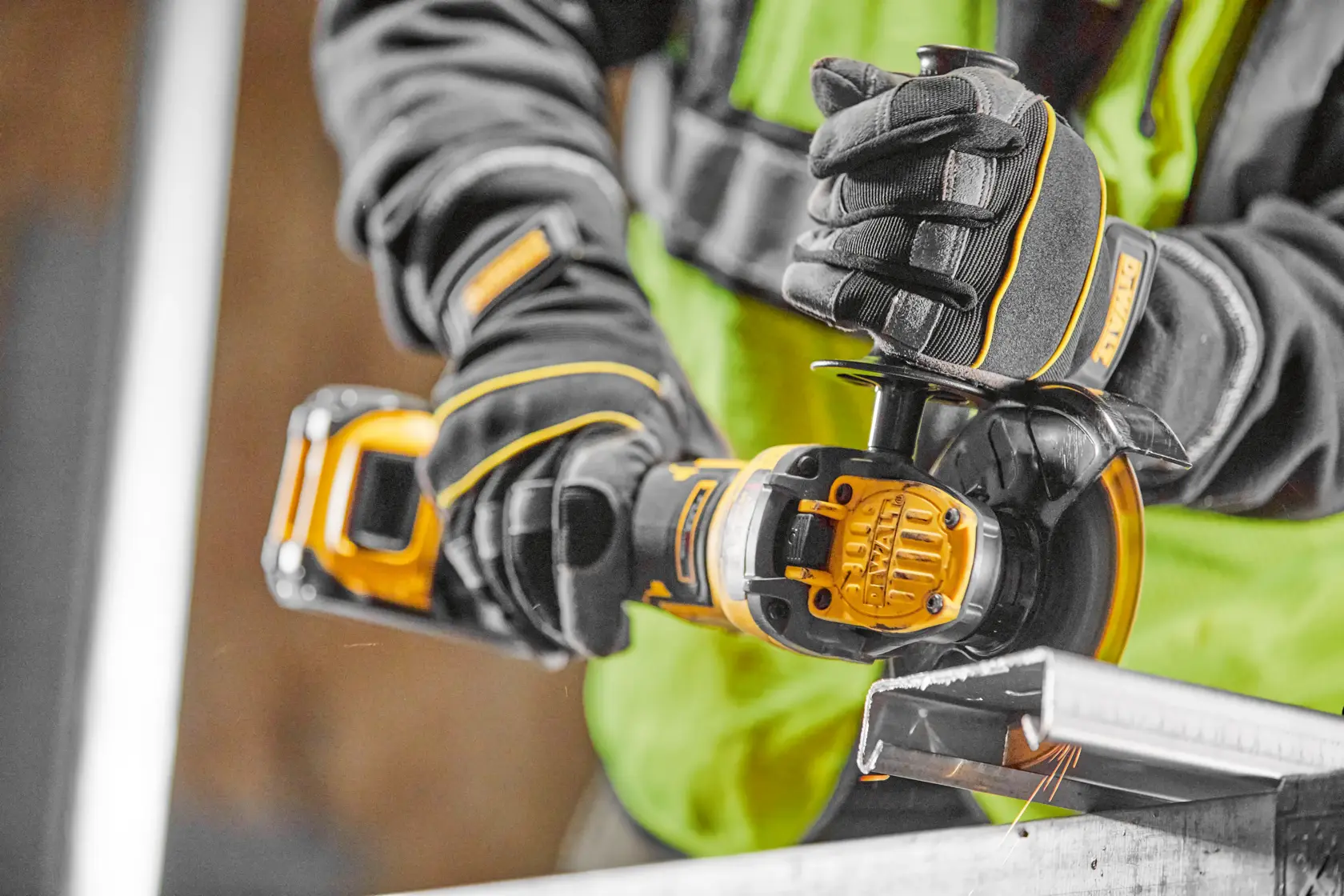 Worker uses a DEWALT cordless angle grinder to cut metal, wearing gloves and safety gear.