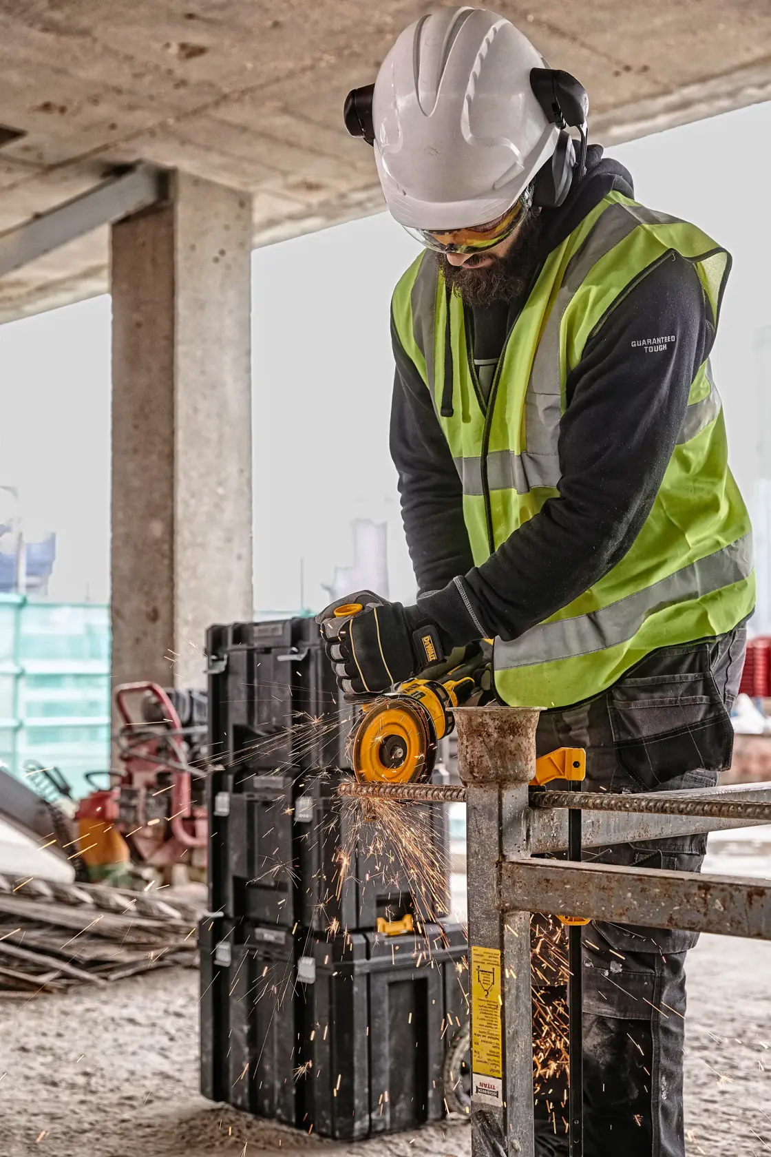 Worker uses a DEWALT grinder, wearing safety gear at a construction site with sparks flying from the tool.