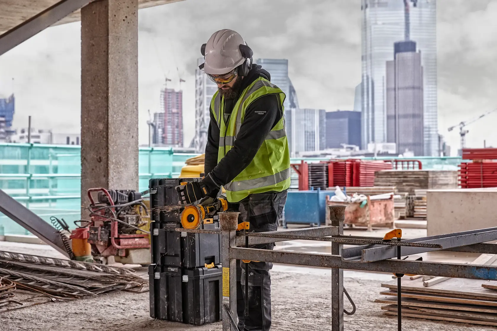 Worker uses DEWALT power tool DCG418T2 on a construction site with city buildings in the background.