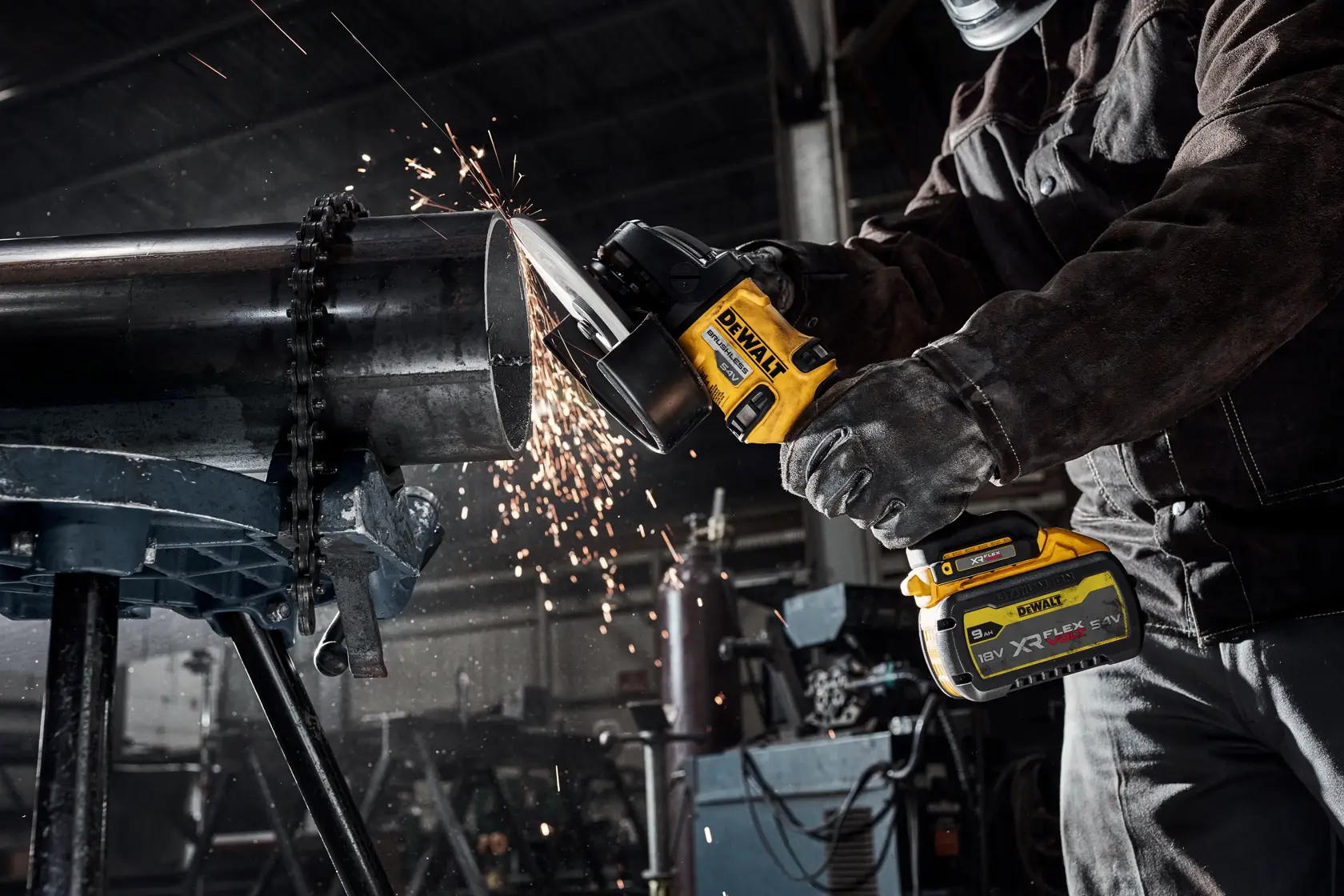 Person uses DEWALT cordless grinder to cut metal pipe, sparks flying in industrial workshop.