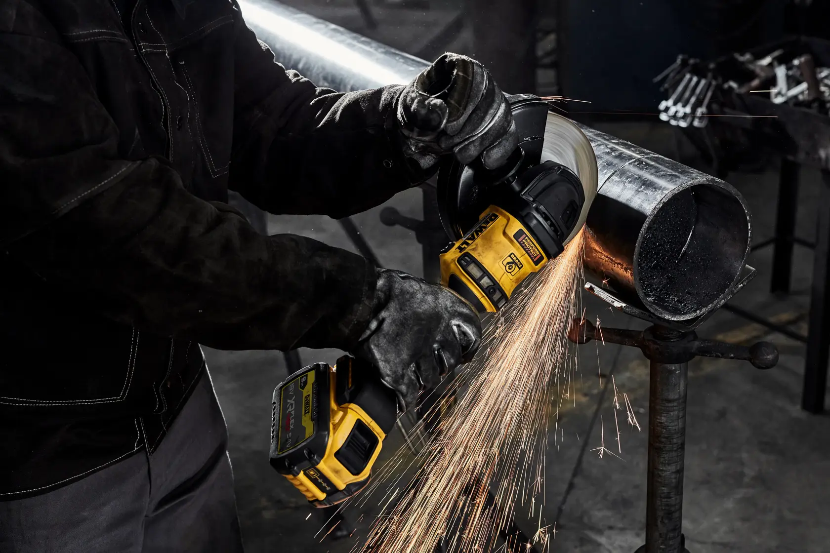 Person using a DEWALT grinder to cut a metal pipe, sparks flying in an industrial setting.