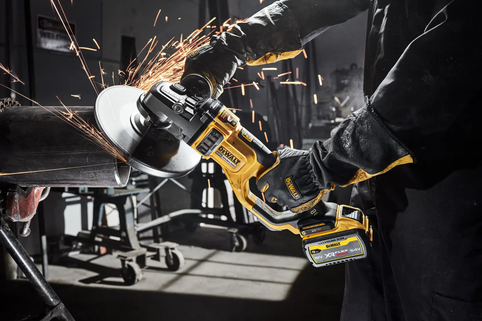 DEWALT cordless grinder cutting metal with sparks in workshop. Worker wearing gloves and protective clothing.