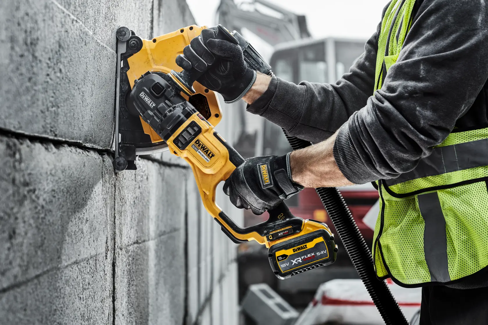 Person using DEWALT cordless wall chaser tool to cut grooves in concrete blocks at a construction site.