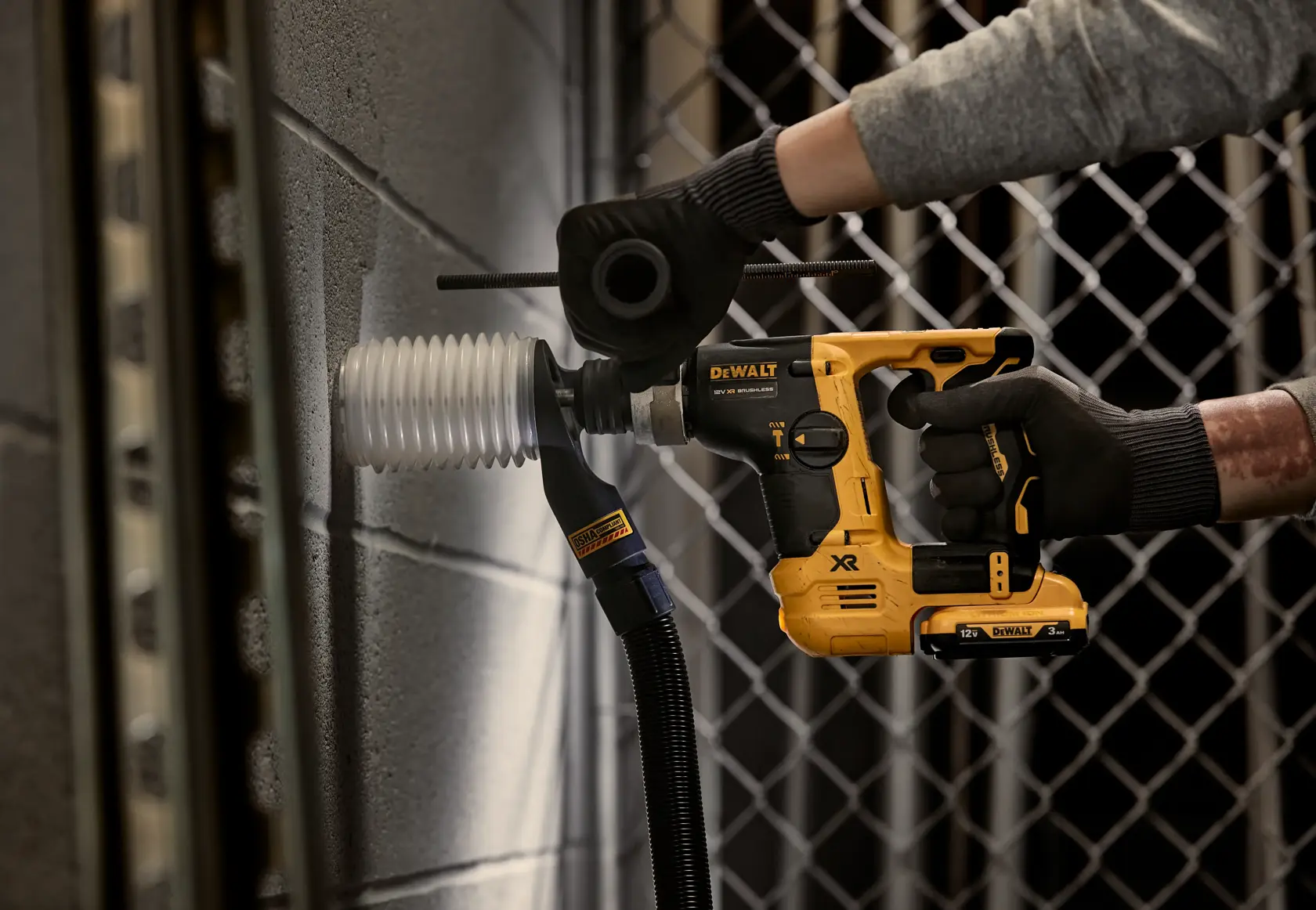 Persona che usa un martello rotante DEWALT su un muro di cemento vicino a un condotto elettrico.