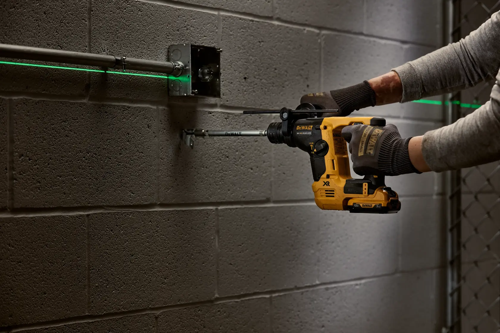 Persona usa un trapano DEWALT a batteria sotto un lavandino per lavori idraulici su muro in mattoni.