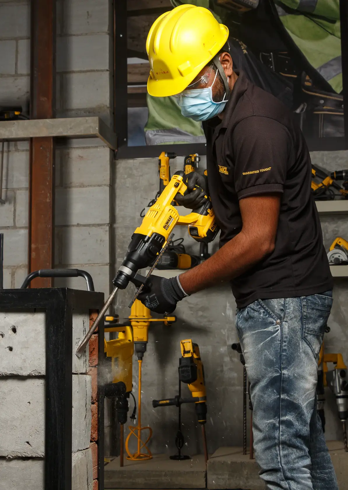 Ouvrier utilise une perceuse DEWALT DCH133NT sur un mur en béton. Équipement et outils visibles.