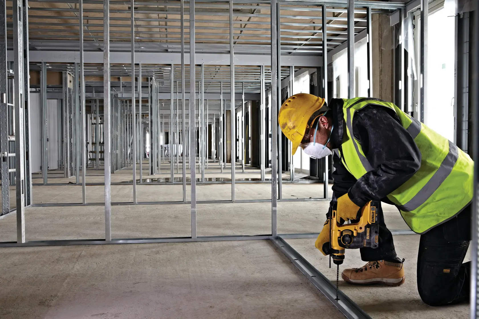 Worker uses DEWALT tool to drill metal frame, wearing safety gear in a building under construction.