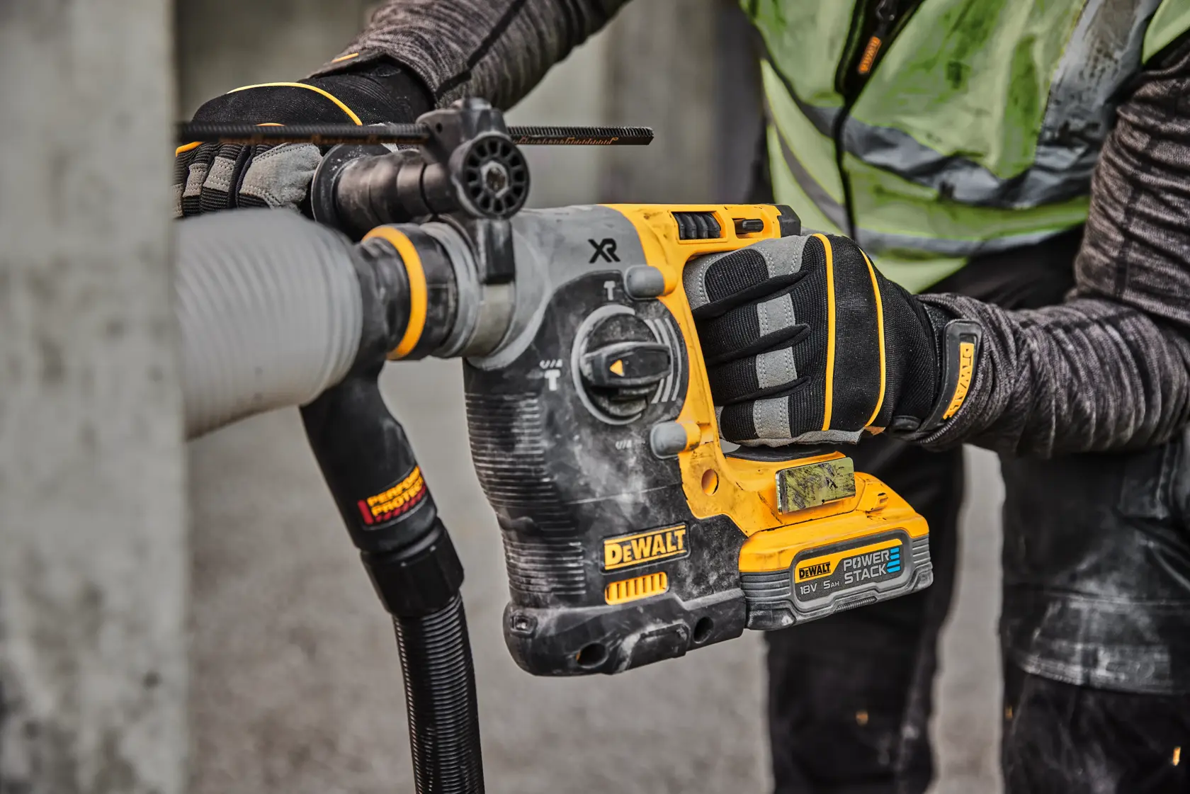Primo piano di un operaio che utilizza un trapano rotativo a batteria DEWALT con batteria POWERSTACK per forare il cemento, indossando guanti e abbigliamento protettivo.