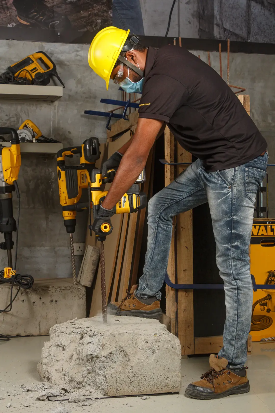 Worker drills concrete block with DEWALT DCH333NT rotary hammer. Wearing safety gear in hardware workshop.