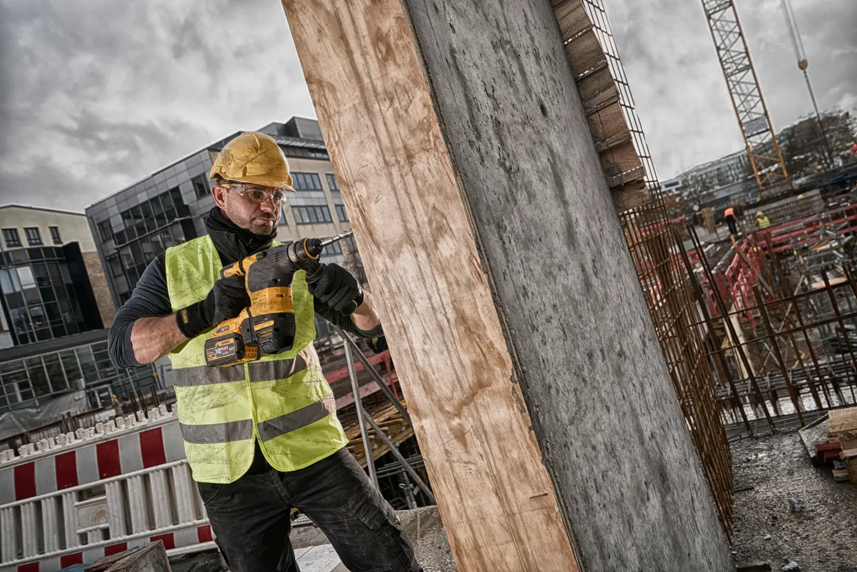 Worker uses DEWALT power tool to drill into concrete at a construction site, wearing helmet and safety vest.
