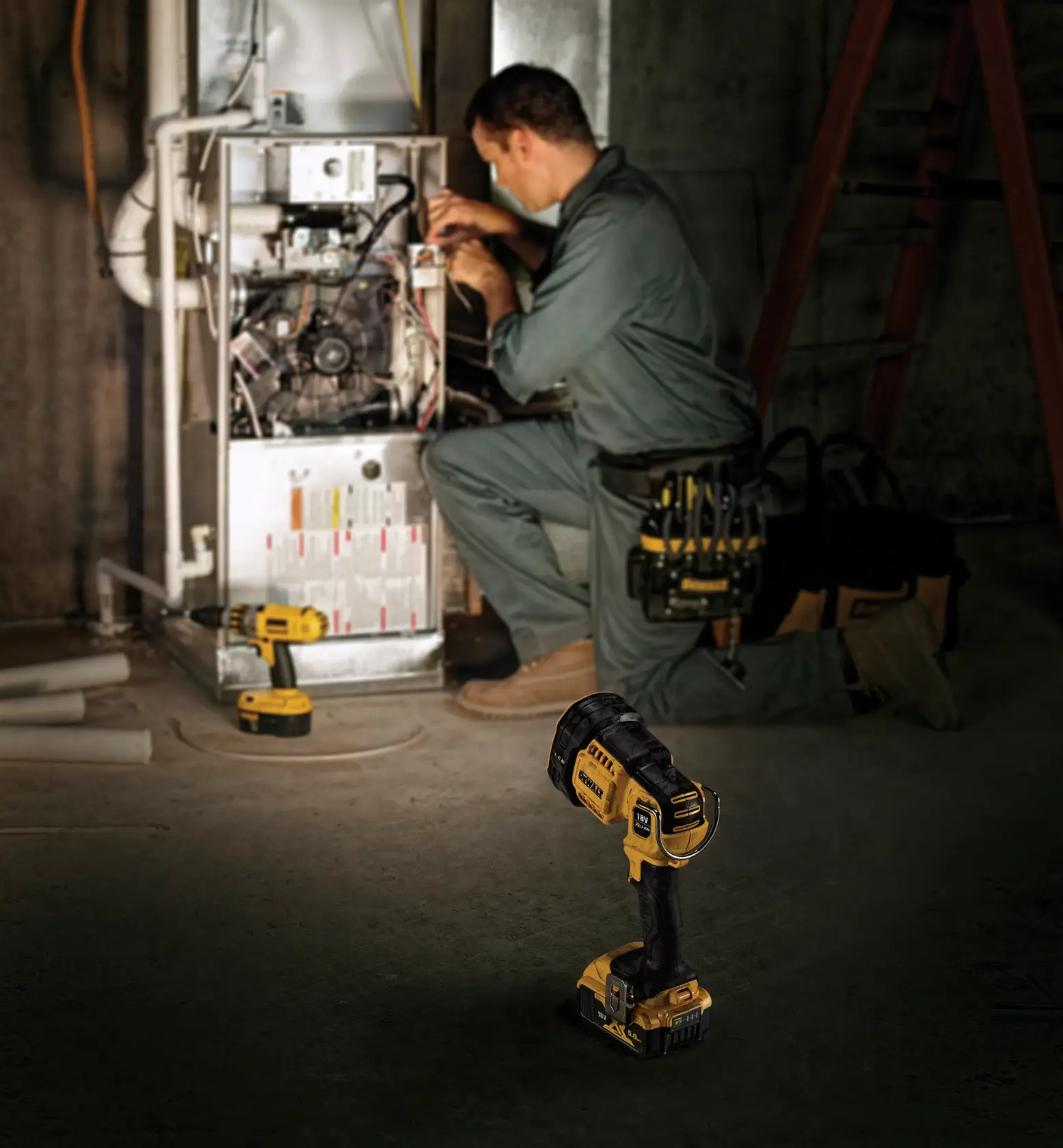En DEWALT DCL043 trådløs LED-spotlight står på betonggulvet i forgrunnen, mens en person i arbeidsklær kneler og utfører vedlikehold på industrimaskiner i bakgrunnen. Andre DEWALT-verktøy og en verktøybag er også synlige.