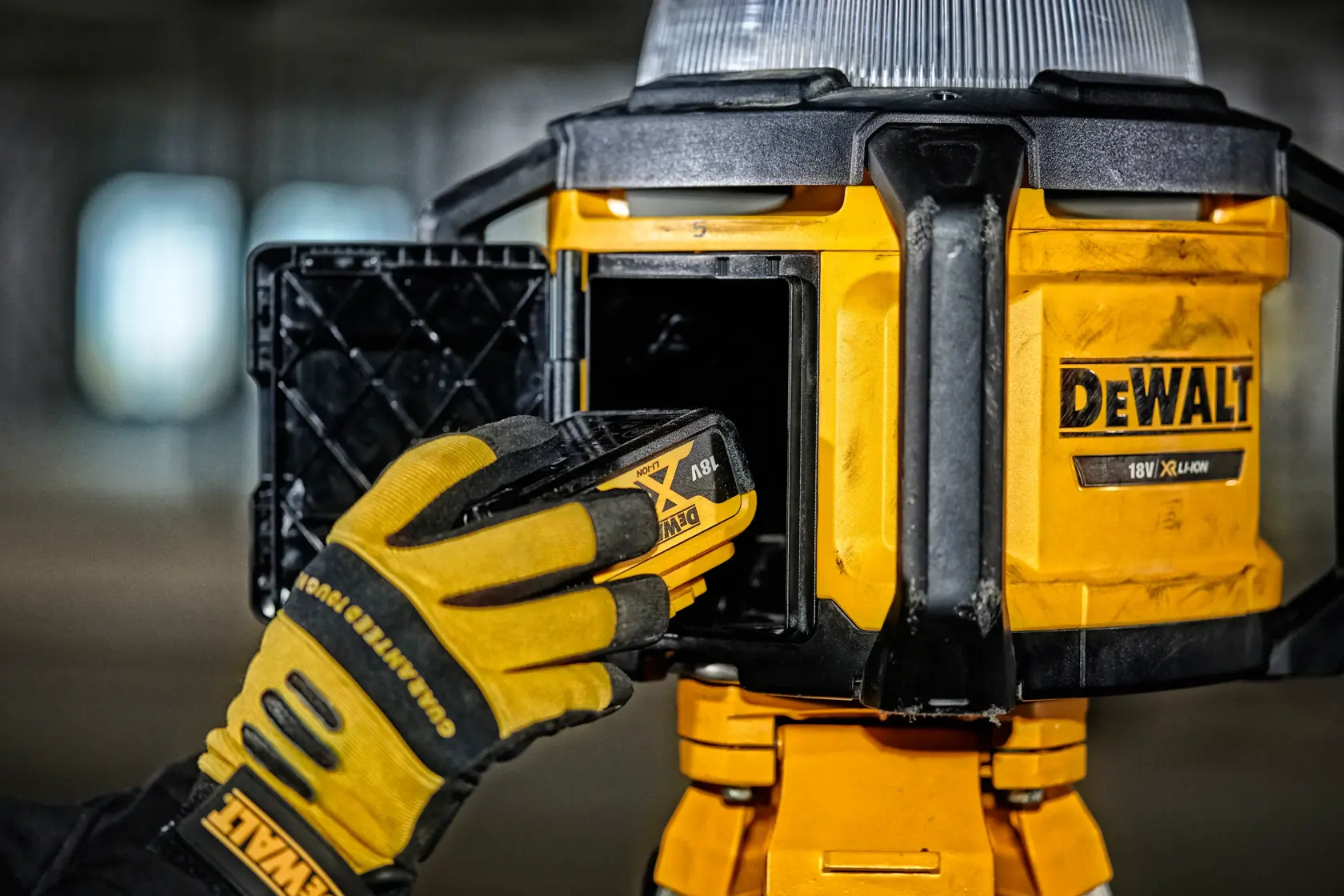 Gloved hand inserts battery into a yellow DEWALT work light. Close-up view of battery compartment and tool.