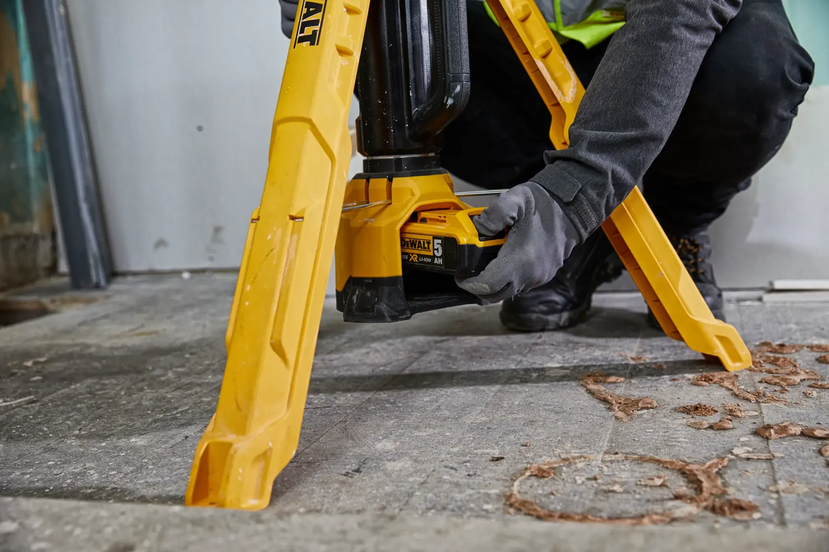 Person installs battery in a yellow DEWALT tripod work light on a workshop floor.