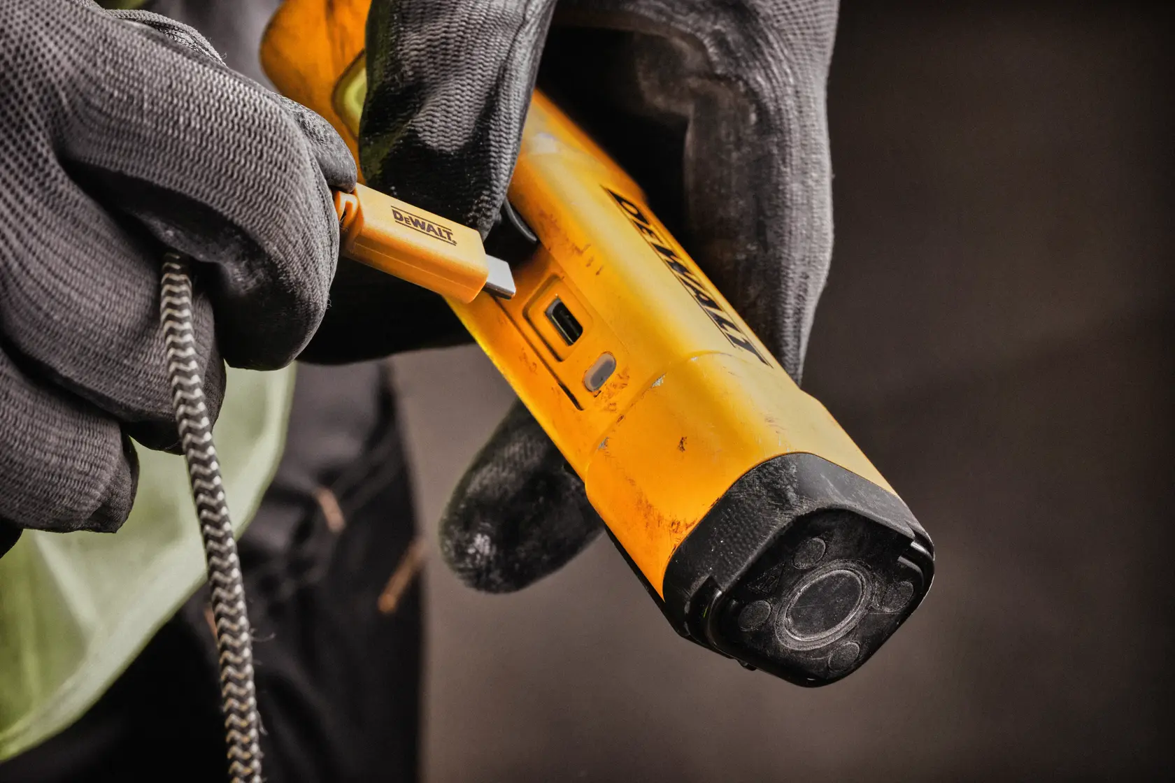 Nærbilde av en hanskekledd hånd som kobler en USB-kabel til en gul DEWALT DCL183 arbeidslampe.