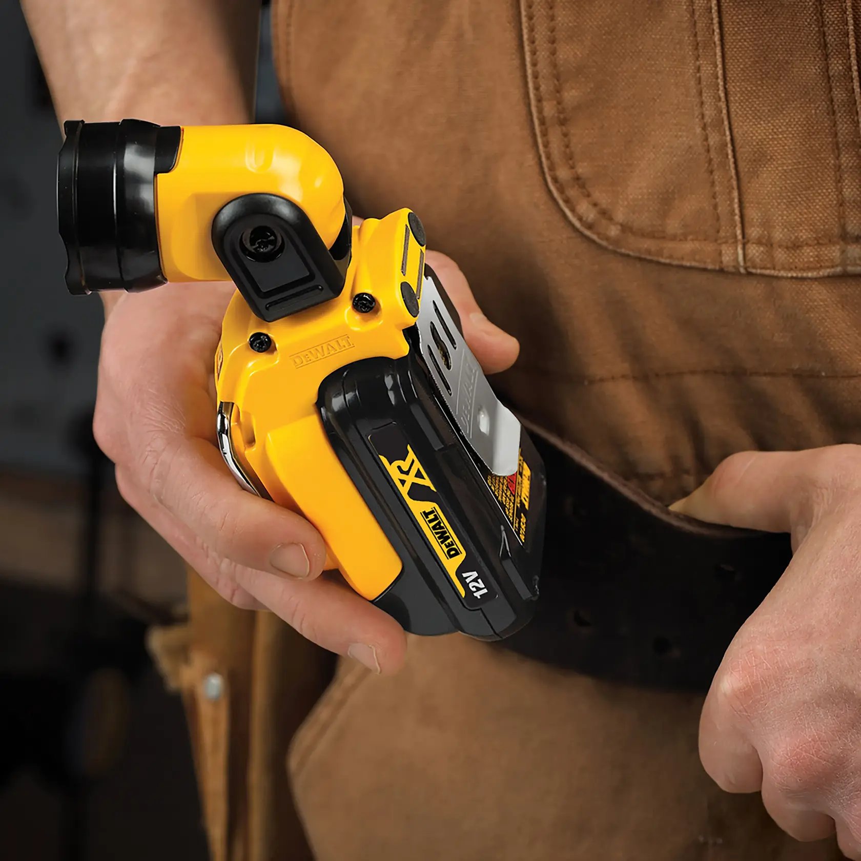 Hand holding a DEWALT DCL510N 12V compact flashlight clipped to a tool belt.
