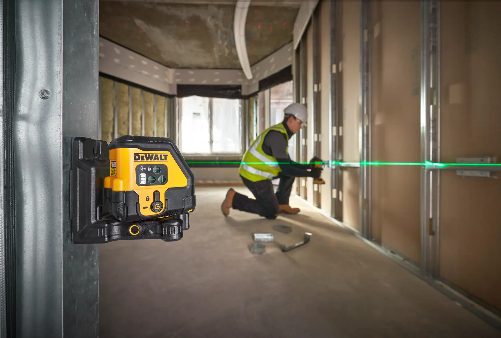 Livella laser DEWALT montata su parete, proietta linea verde mentre un operaio allinea i materiali.