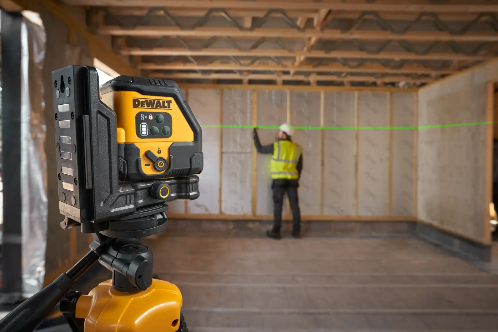 Livella laser DEWALT su treppiede proietta linea verde in cantiere con operatore che segna la parete.