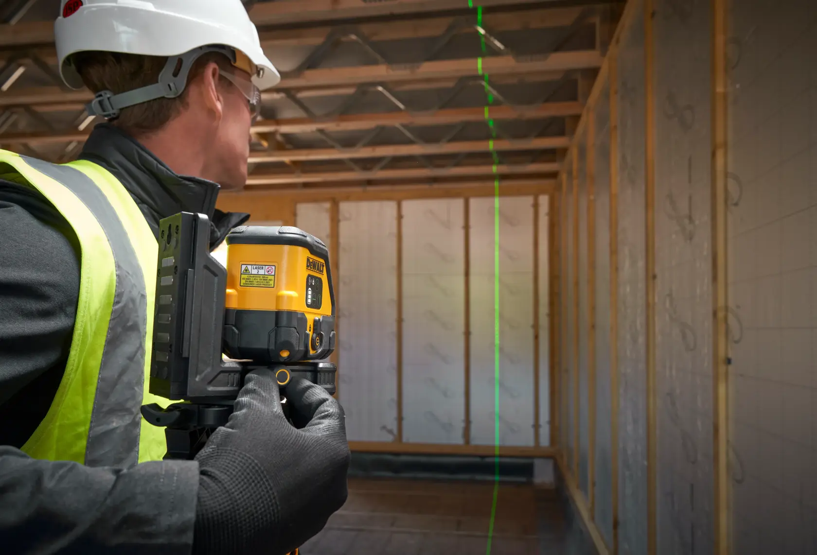 Operaio usa livello laser DEWALT, proietta una linea verde verticale in edificio non finito.