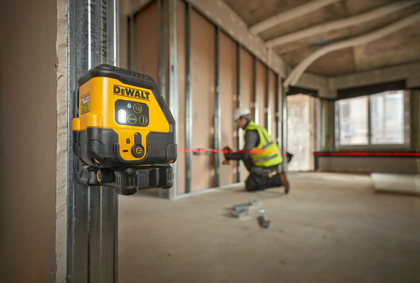 Livella laser DEWALT su telaio metallico. Un lavoratore allinea i materiali con linea laser rossa.