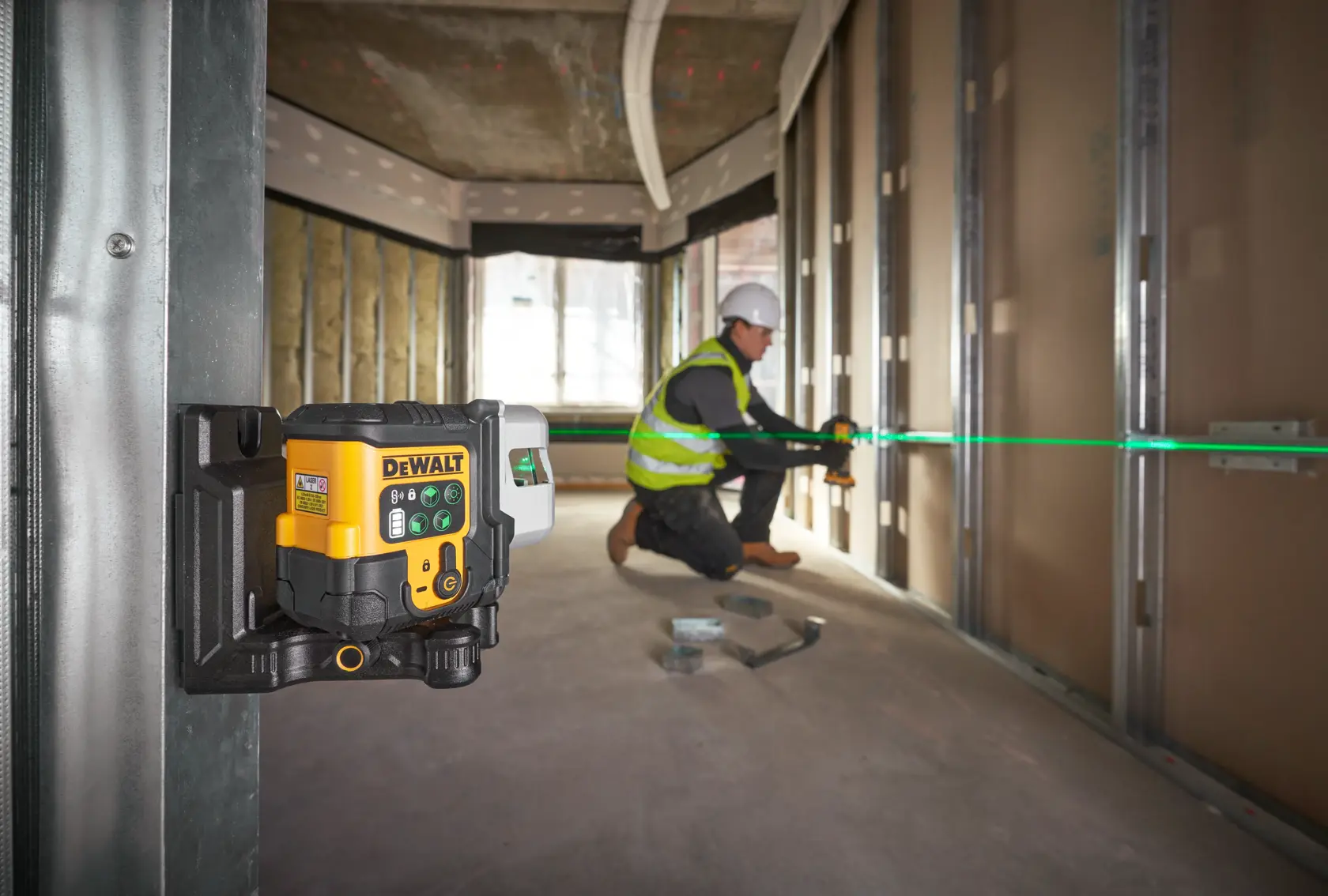 Livella laser DEWALT su treppiede proietta linea verde, operaio segna parete in cantiere.