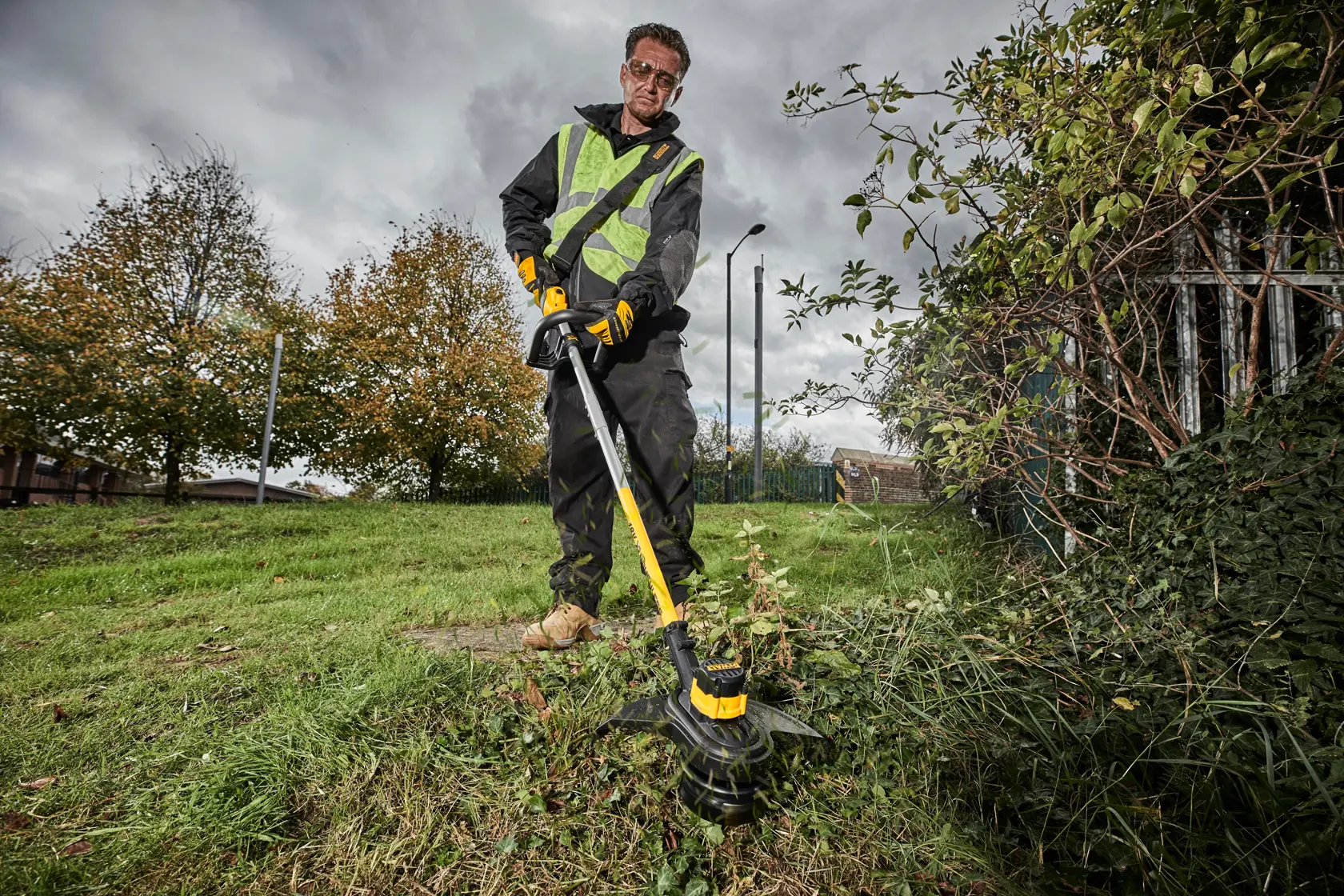 Persona usa un tagliaerba DEWALT all’aperto, con guanti da lavoro e giubbotto di sicurezza.