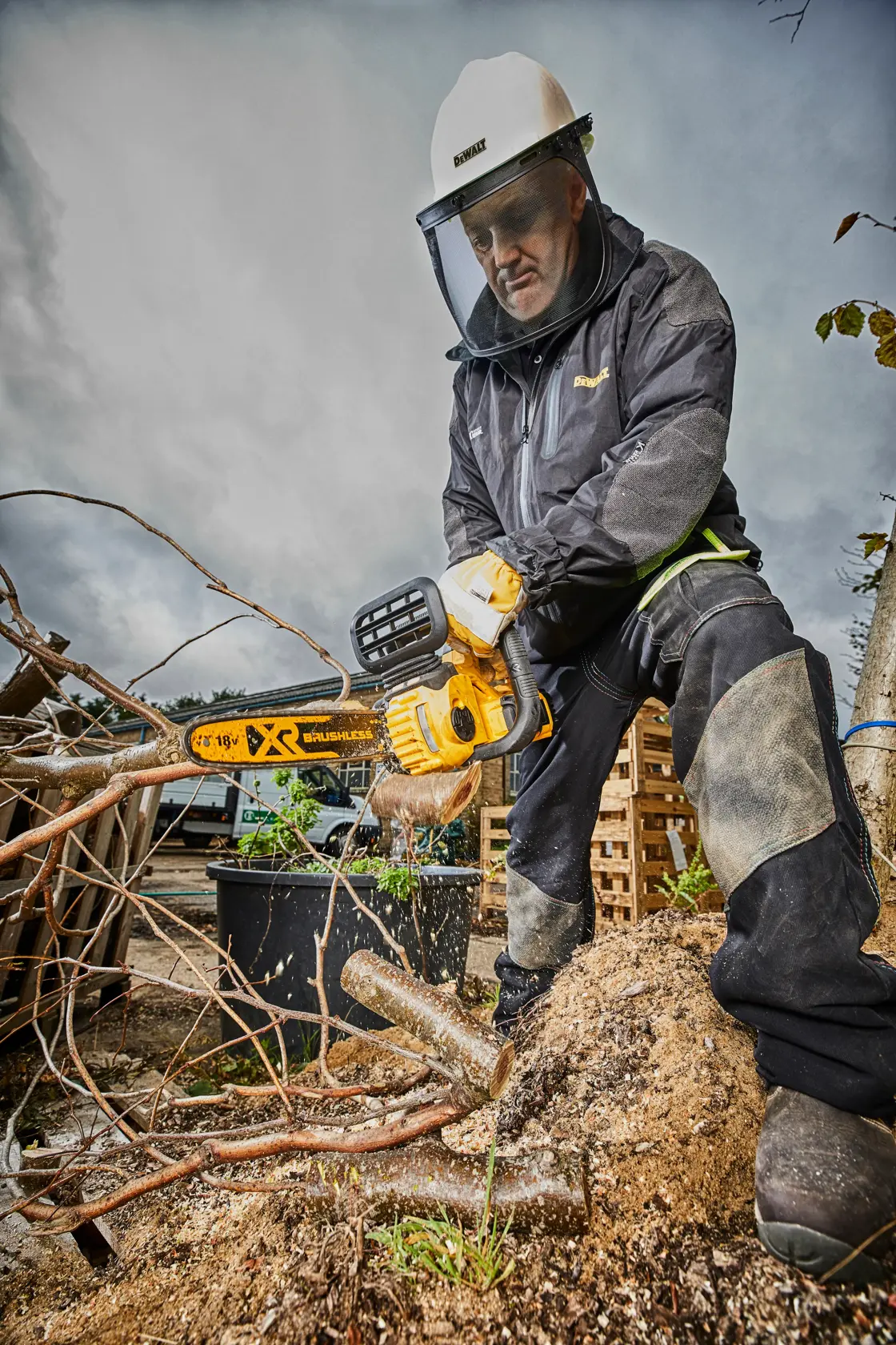 Person uses DEWALT chainsaw DCM565N to cut tree branches outdoors, wearing safety gear.