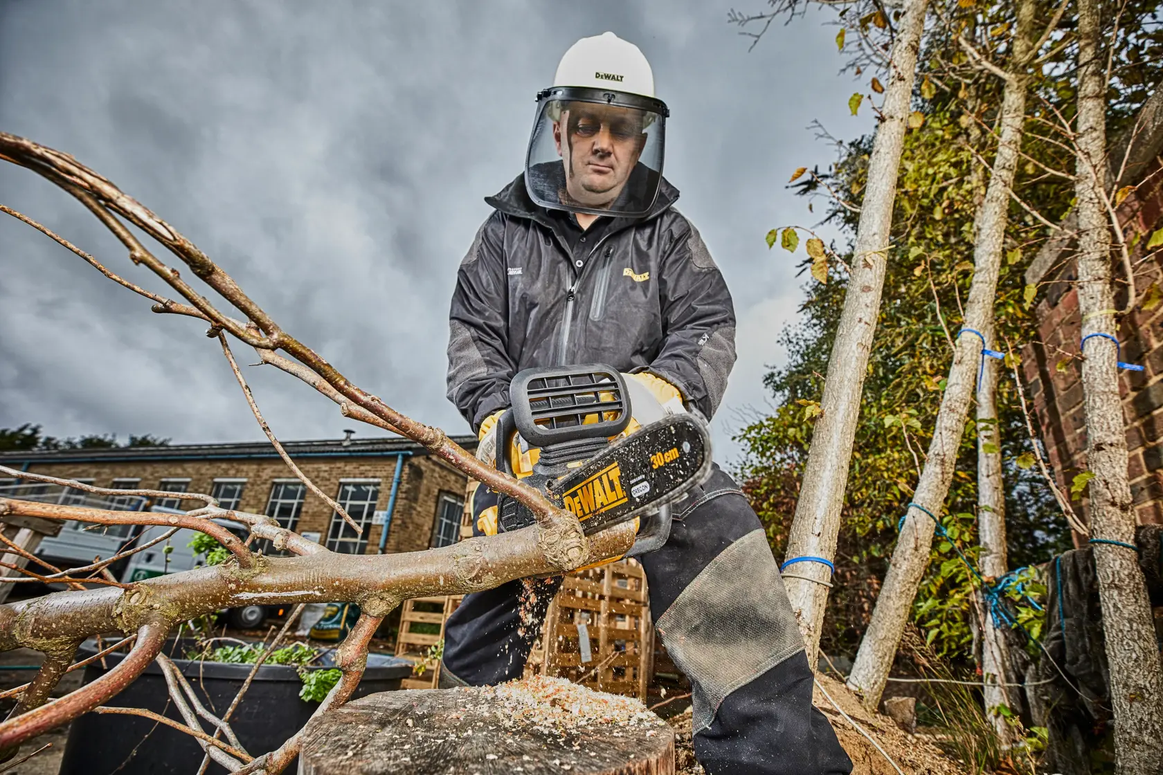 Person using a DEWALT chainsaw outdoors, cutting a tree branch while wearing protective gear.