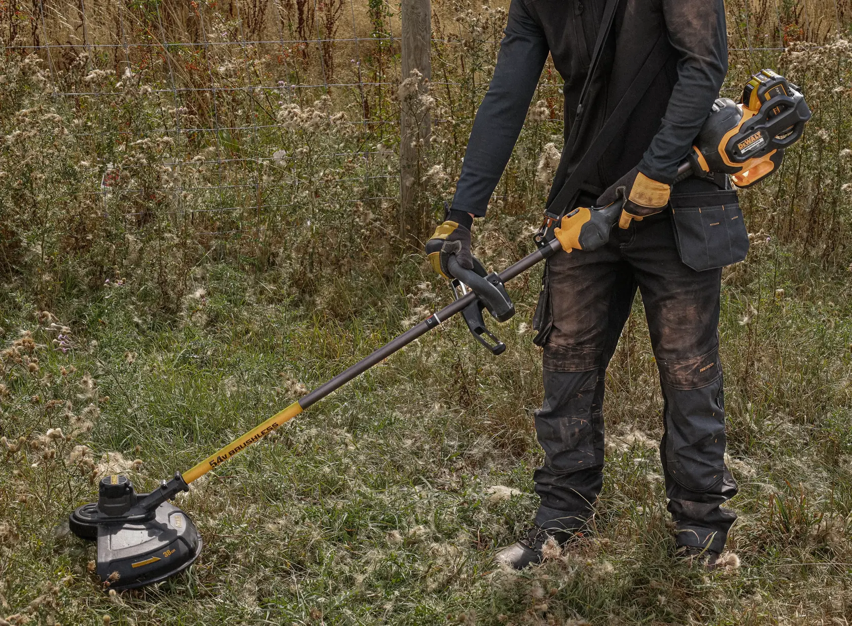 Person using a DEWALT cordless brush cutter outdoors on grassy terrain.