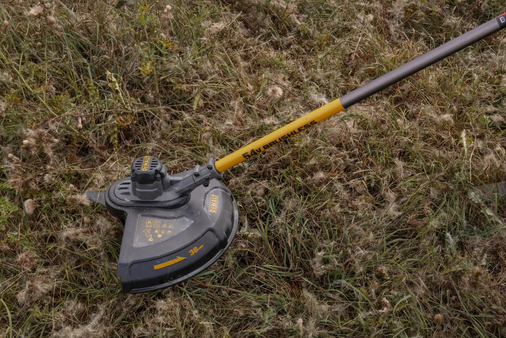 DEWALT brushless cordless grass trimmer with yellow shaft on tall grass outdoors.