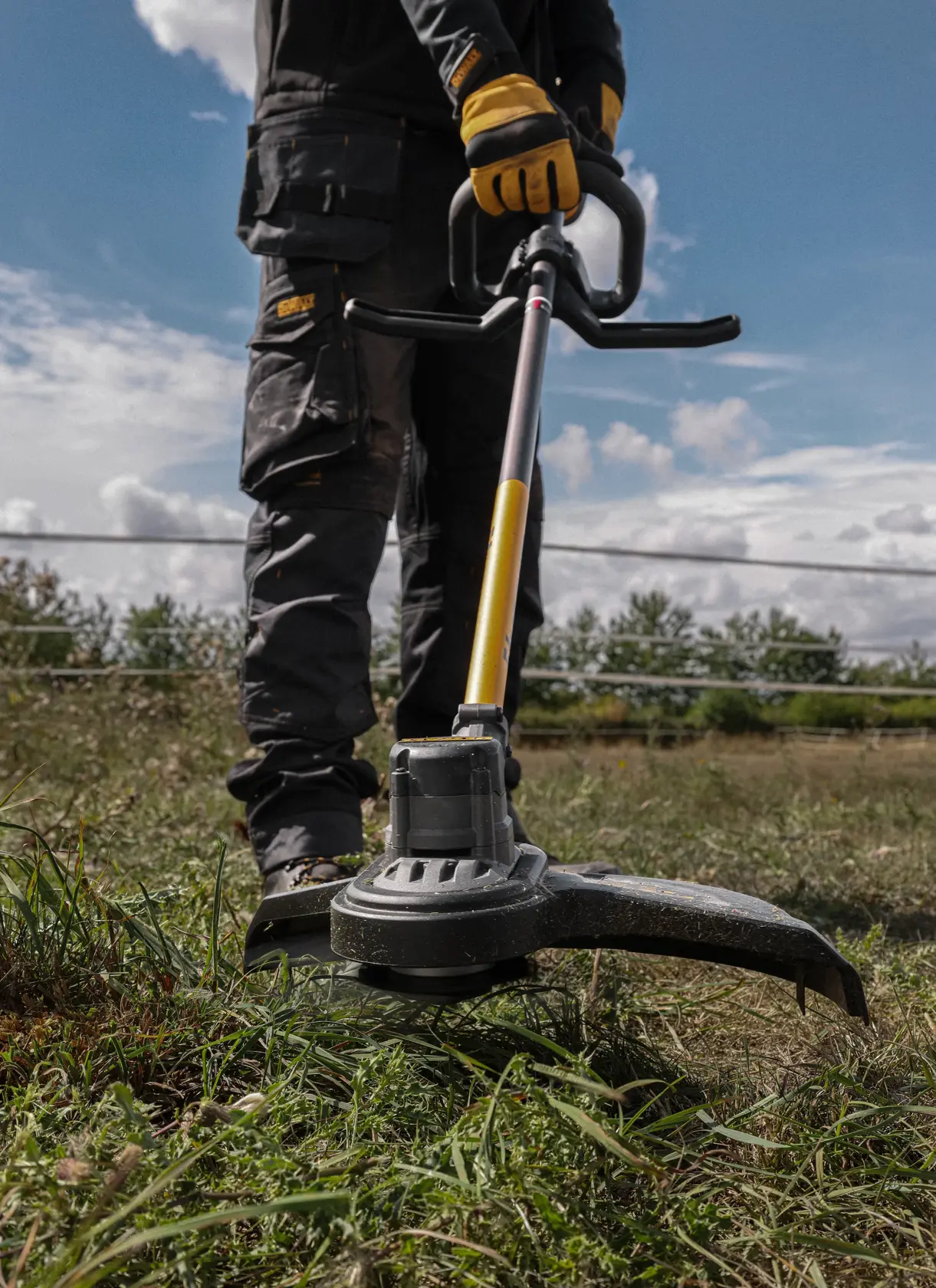 Person using a DEWALT cordless trimmer in tall grass outdoors.