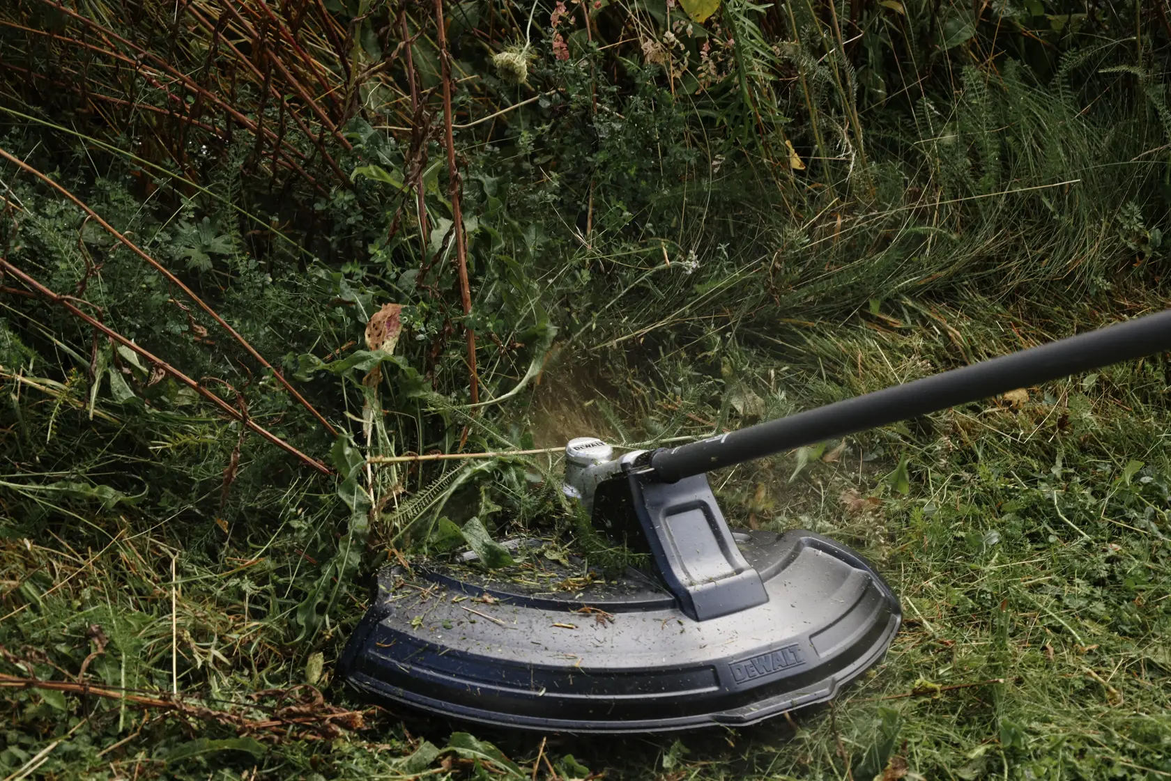 DEWALT brushcutter trimming grass. Shown DCMASST1N, DCZ65713X1-XE, DCMASST1N-XJ Photography SKU.