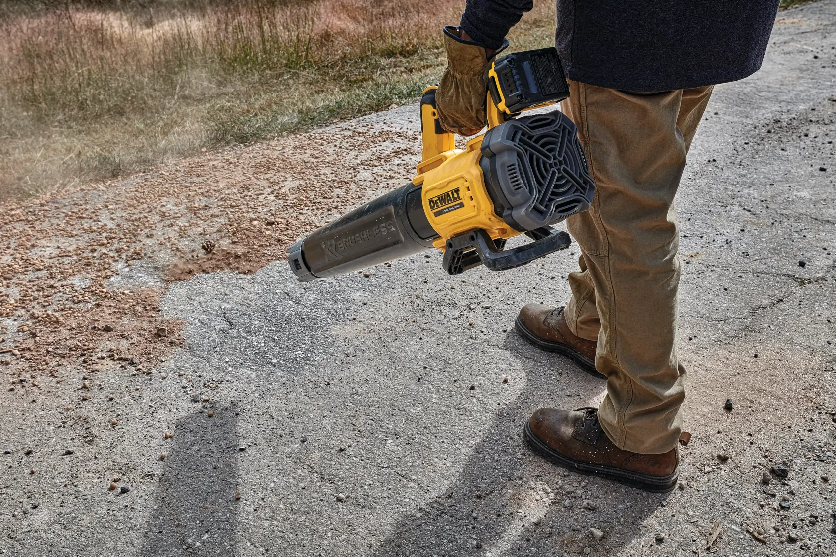 Person using a DEWALT cordless blower to clear debris from a paved outdoor surface.