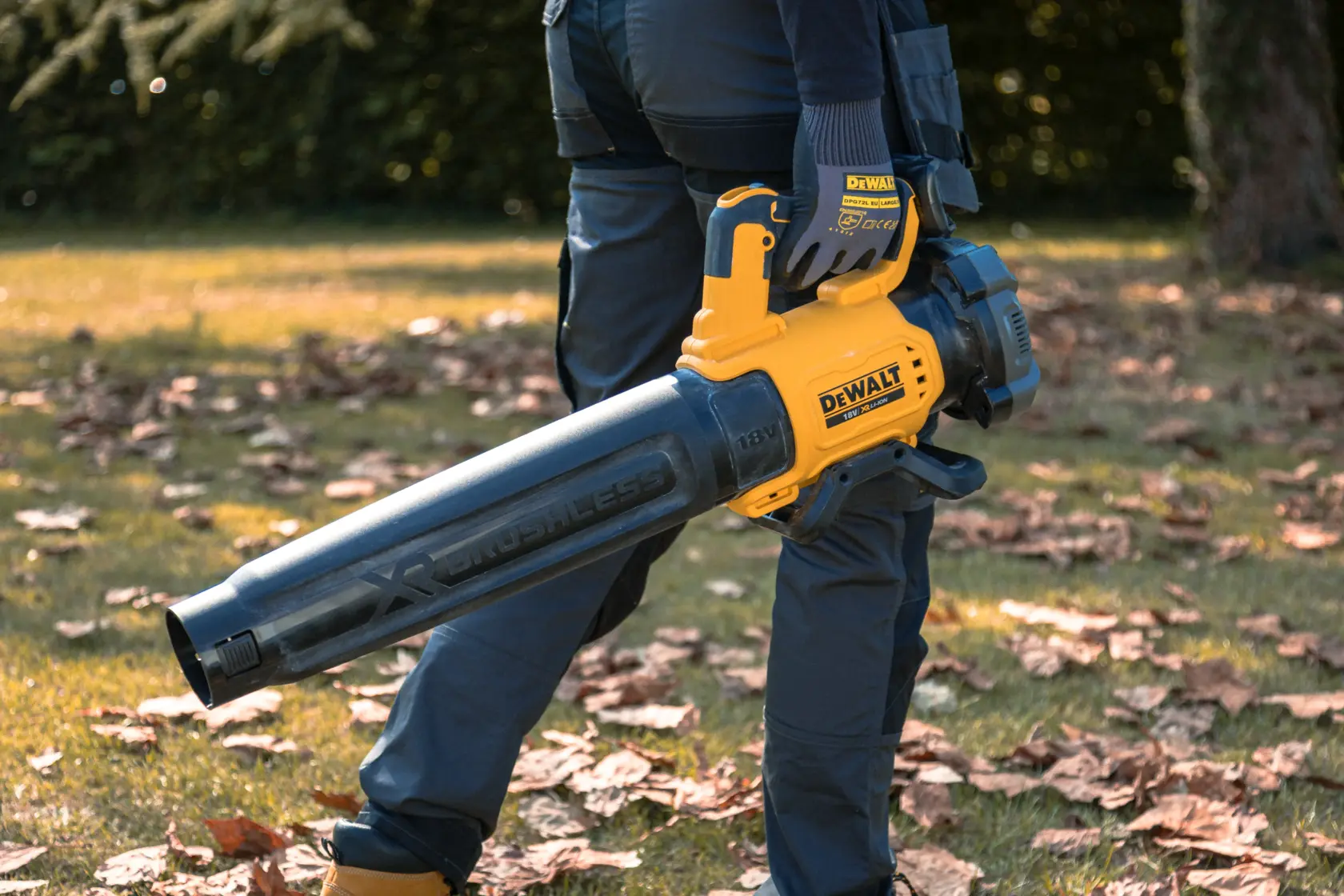 Person holds DEWALT cordless leaf blower outdoors, surrounded by fallen leaves on grass.