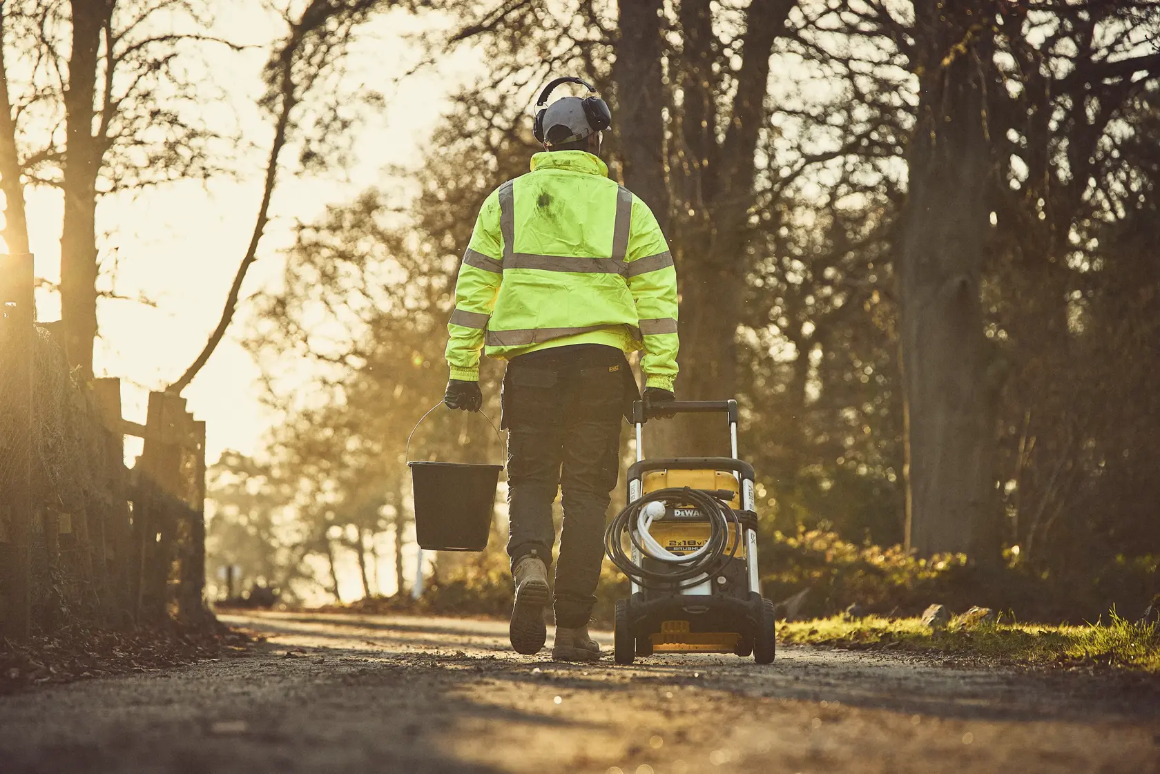 A person uses a DEWALT cordless pressure washer outdoors, spraying water on the ground.