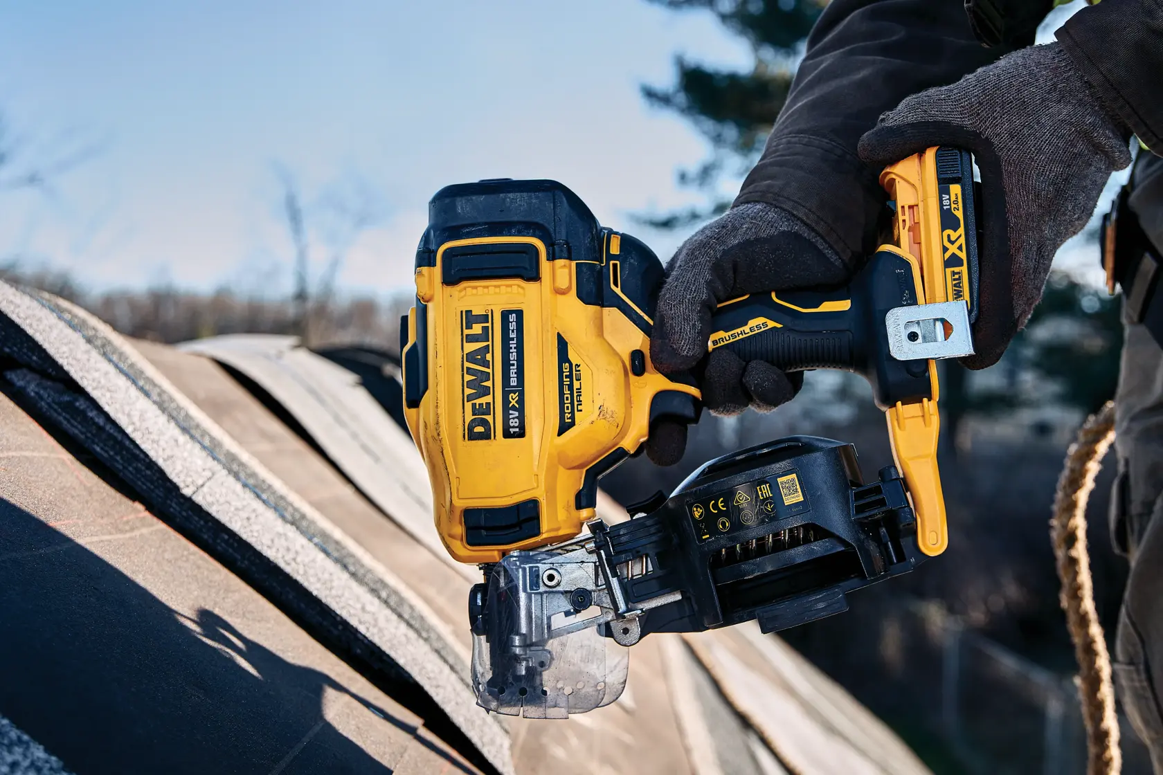 Person using DEWALT cordless roofing nailer on a roof outdoors, wearing gloves.