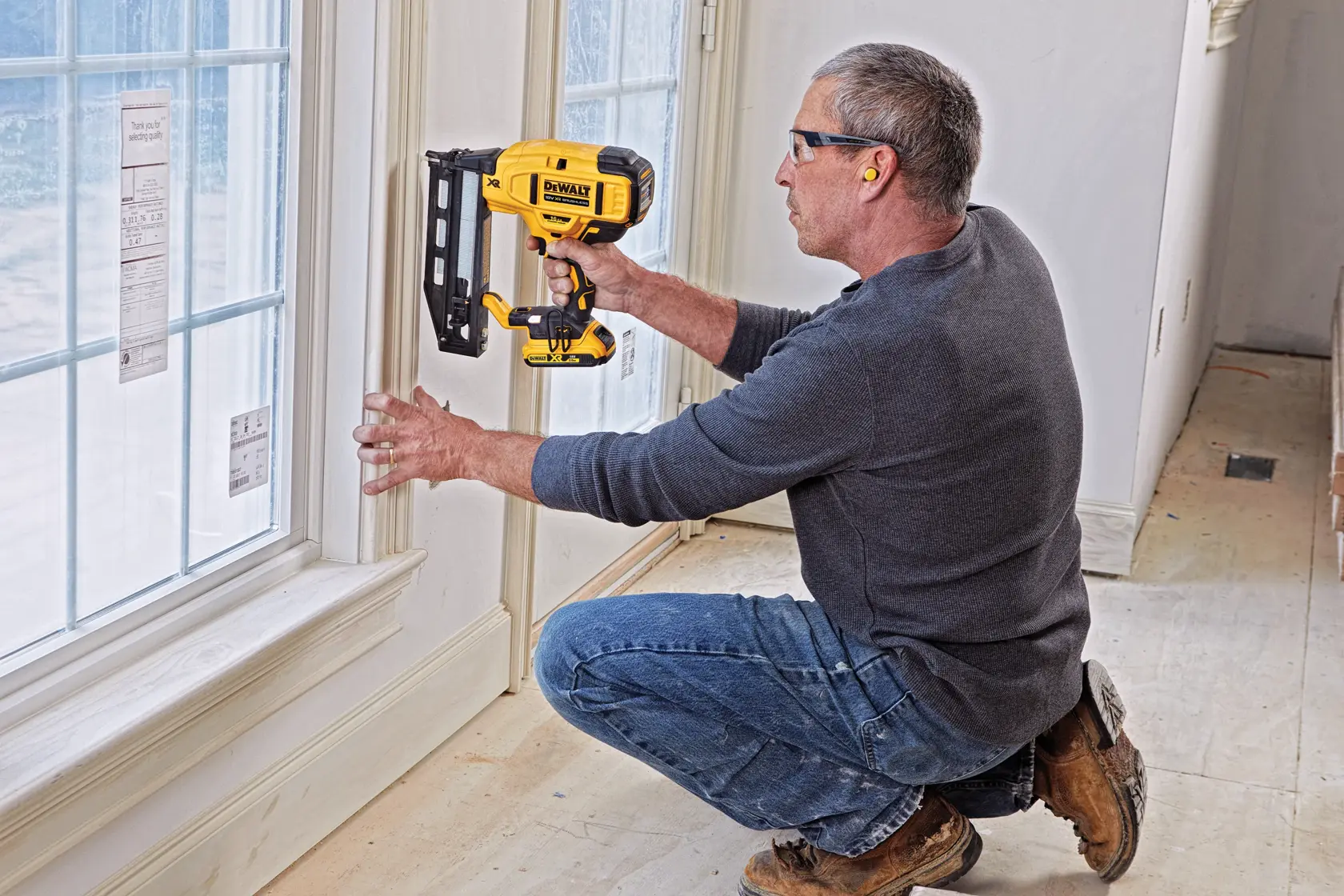 Person uses a DEWALT nailer to attach trim near a window during interior construction.