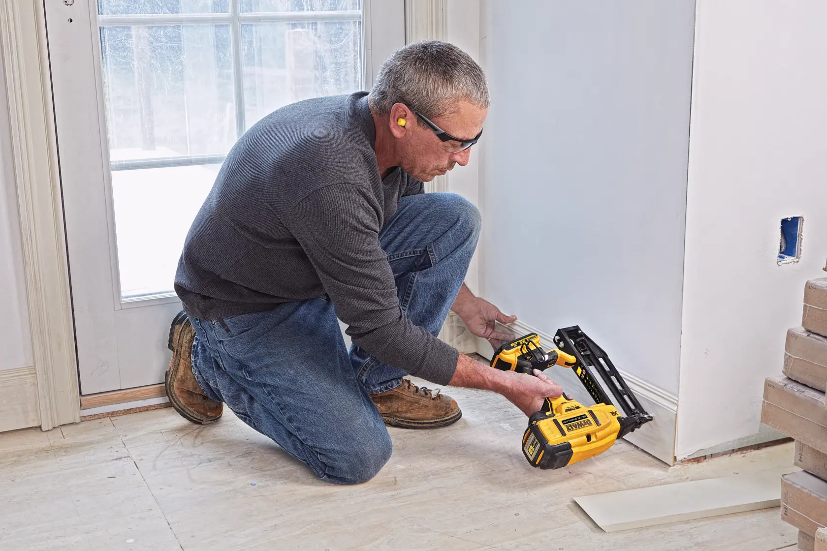 Person using a DEWALT nailer to attach baseboard near a door frame in a room under renovation.