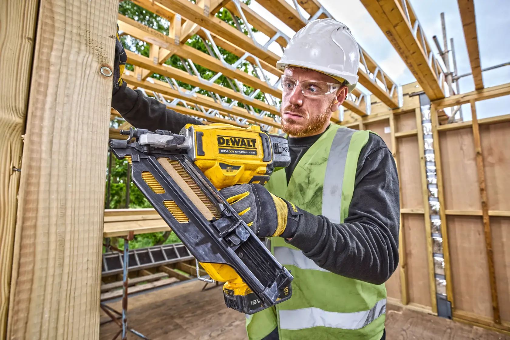 Person using a DEWALT DCN930N nailer in construction, wearing safety gear and working with wooden beams.