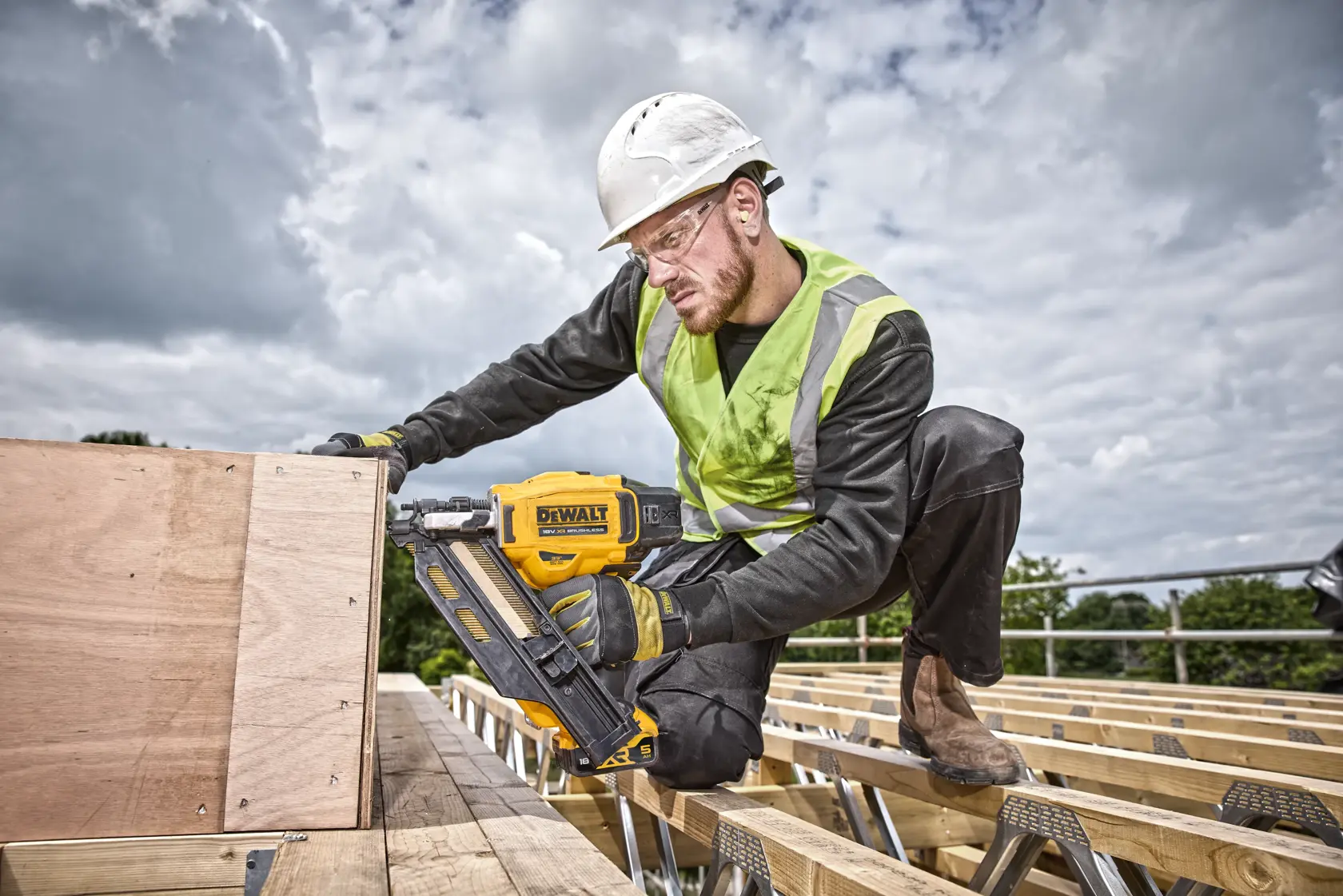 Worker uses a DEWALT DCN930P2 nailer outdoors, fastening wood on a construction site.