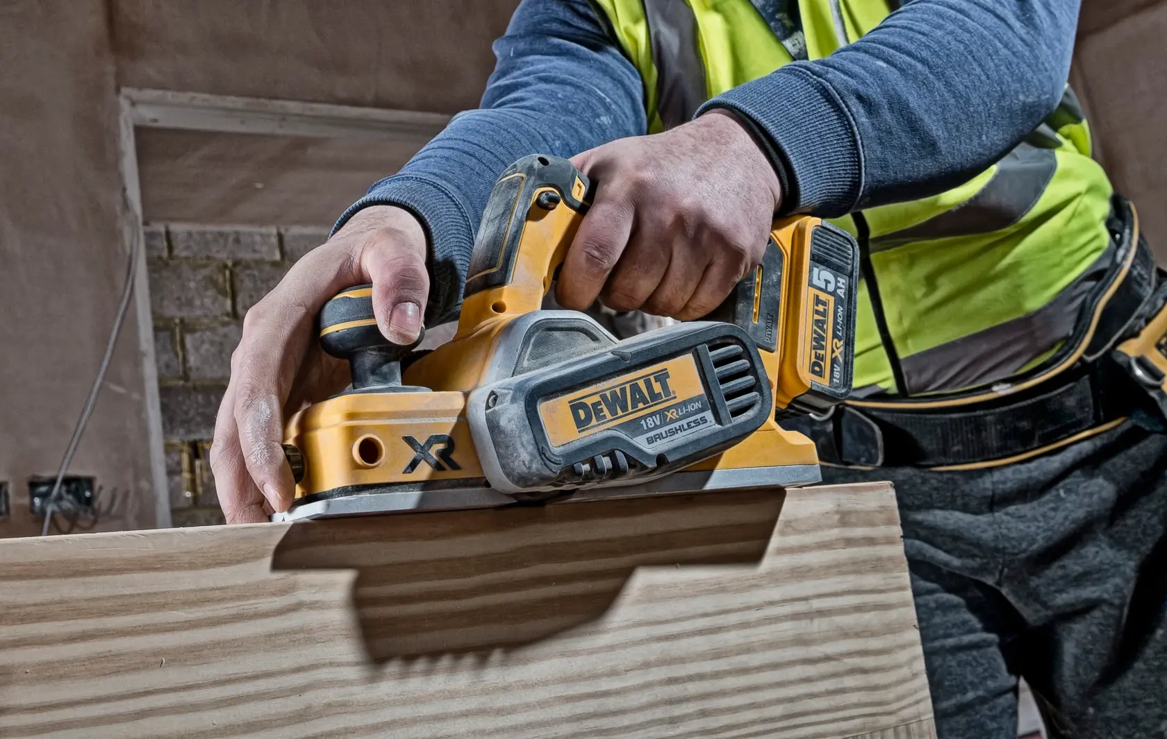 Person using a DEWALT DCP580N cordless planer on a wooden surface at a construction site.