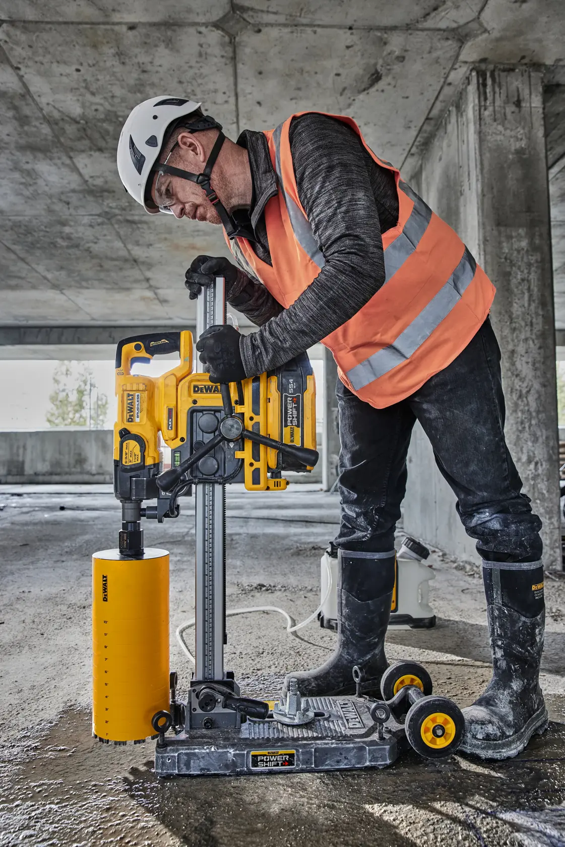 Worker uses a DEWALT DCPS151 core drill on a construction site. He wears safety gear and operates the yellow tool.