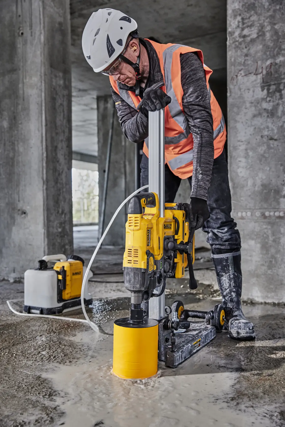 A worker uses a DEWALT DCPS151 core drill on a wet concrete floor at a construction site.