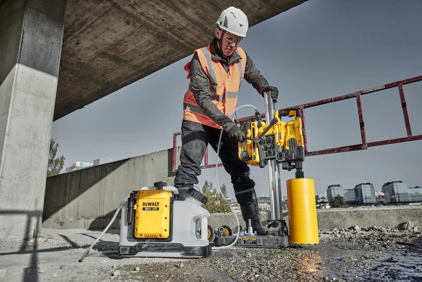 Worker uses DEWALT DCPS151 core drill on concrete at construction site, wearing safety helmet and vest.