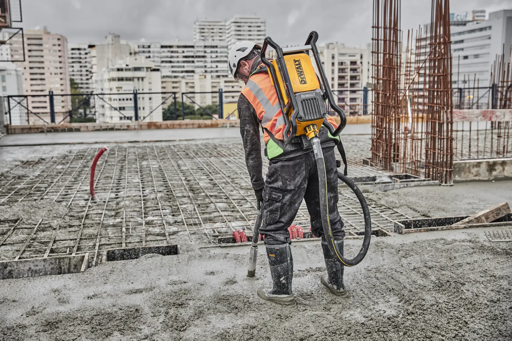 Worker uses DEWALT concrete tool on construction site, wearing safety gear and boots.