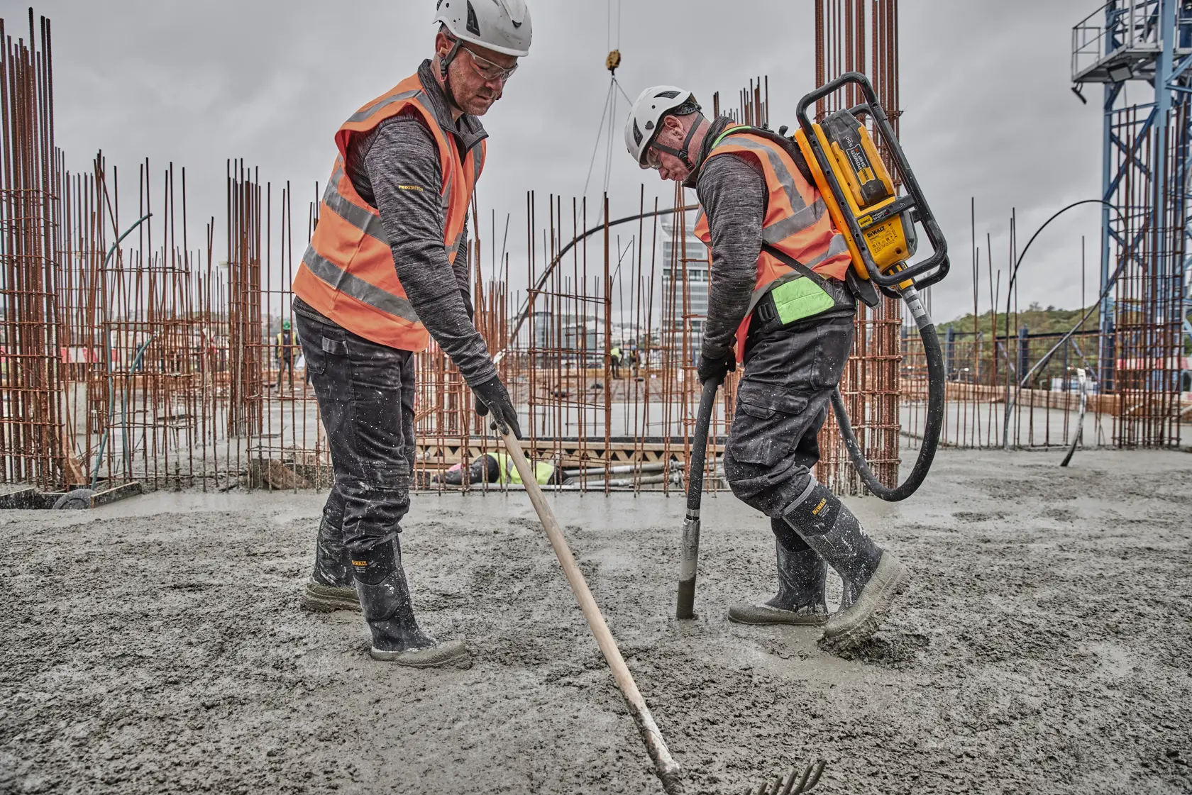 Two workers in safety gear use DEWALT equipment while working with concrete at a construction site.