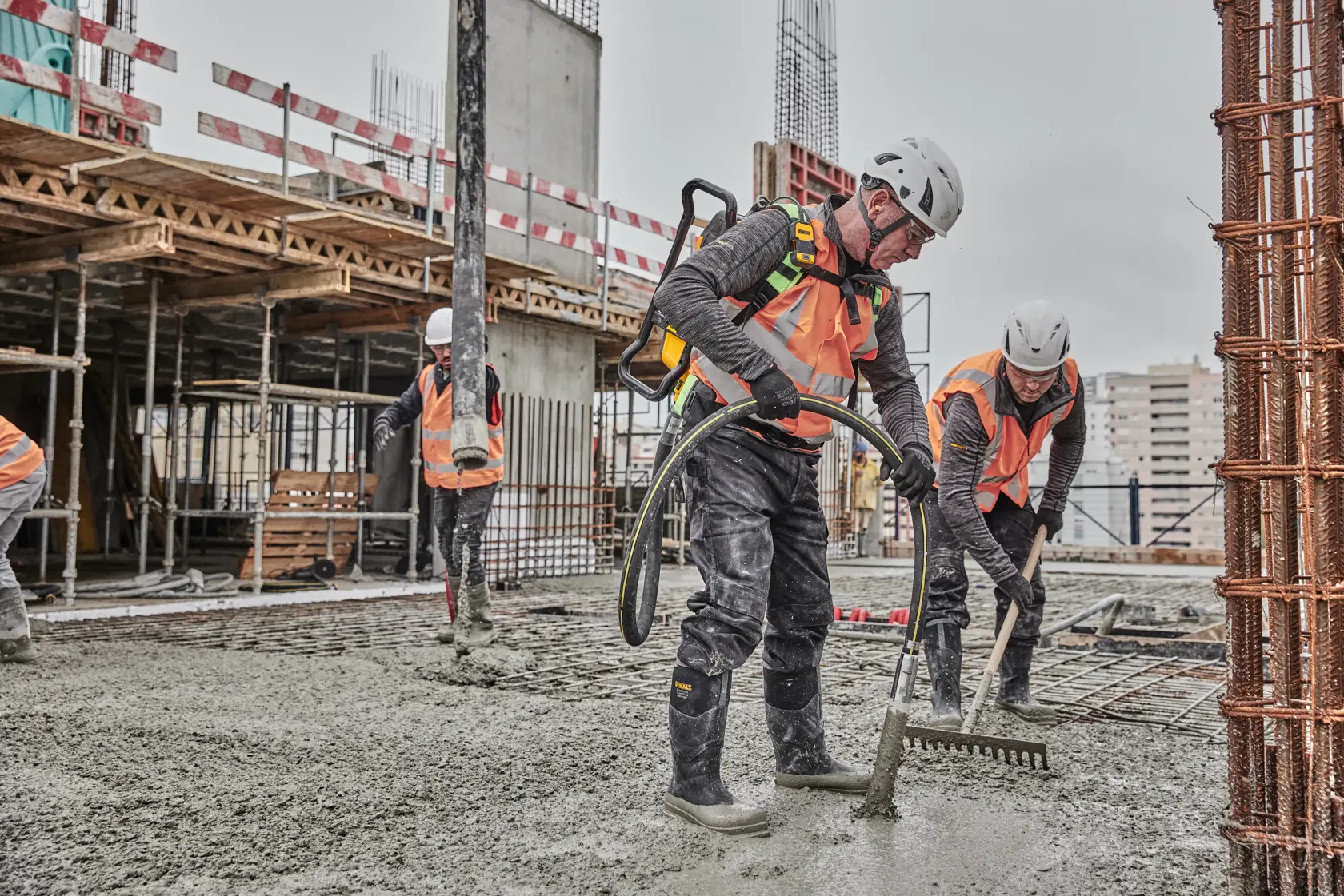 Workers in safety gear spread wet concrete at a construction site with tools and equipment.