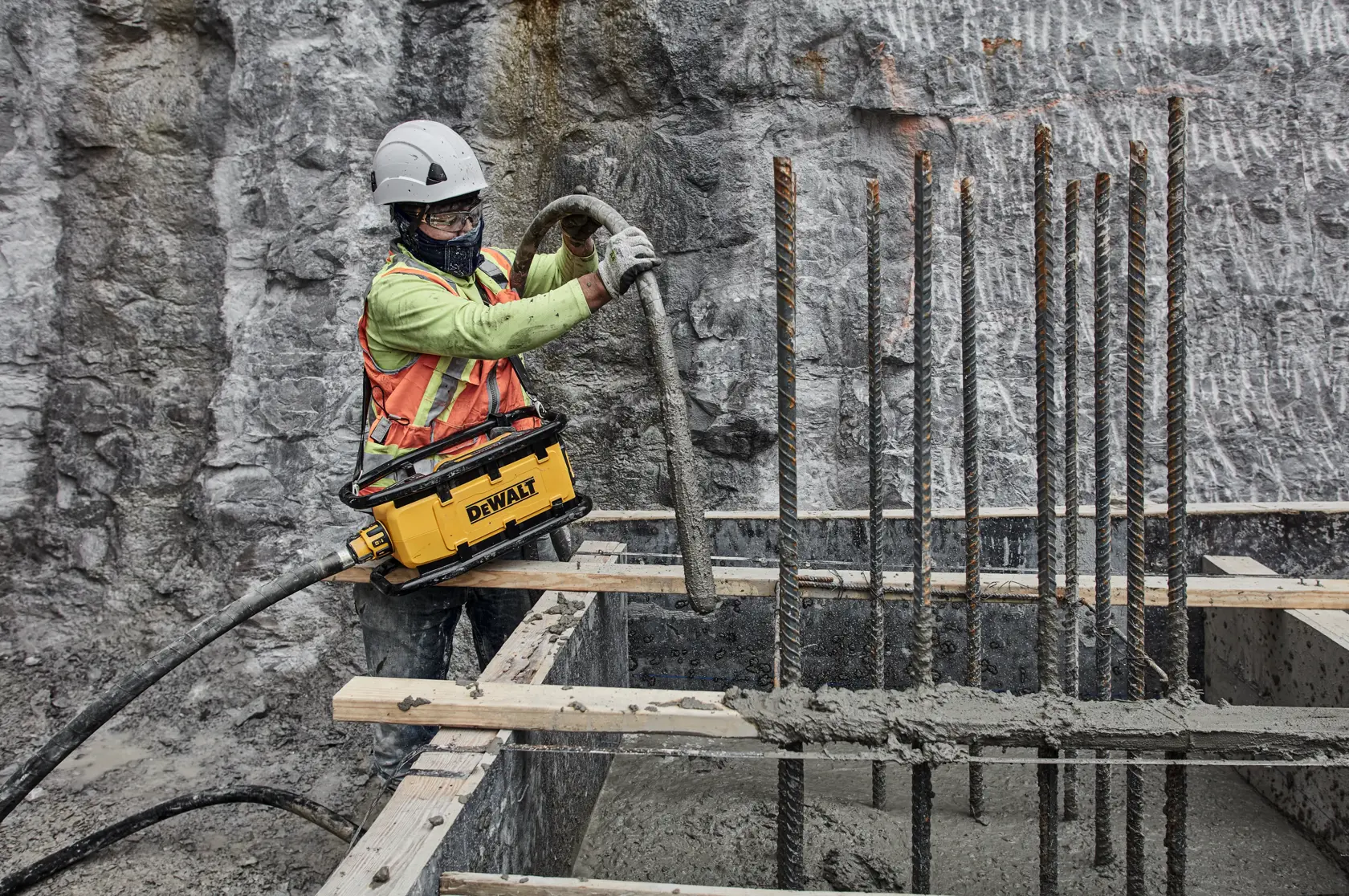 Worker using DEWALT tool for concrete work at construction site with rebar and safety gear.