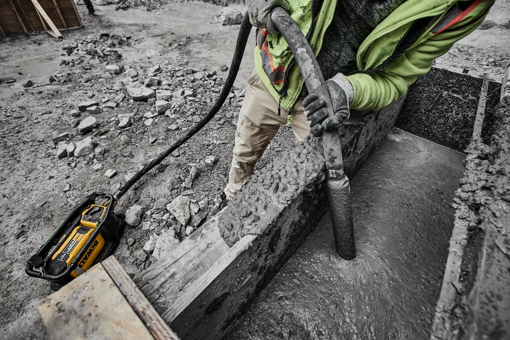 DEWALT concrete vibrator used by worker on construction site, smoothing wet concrete inside a wooden form.