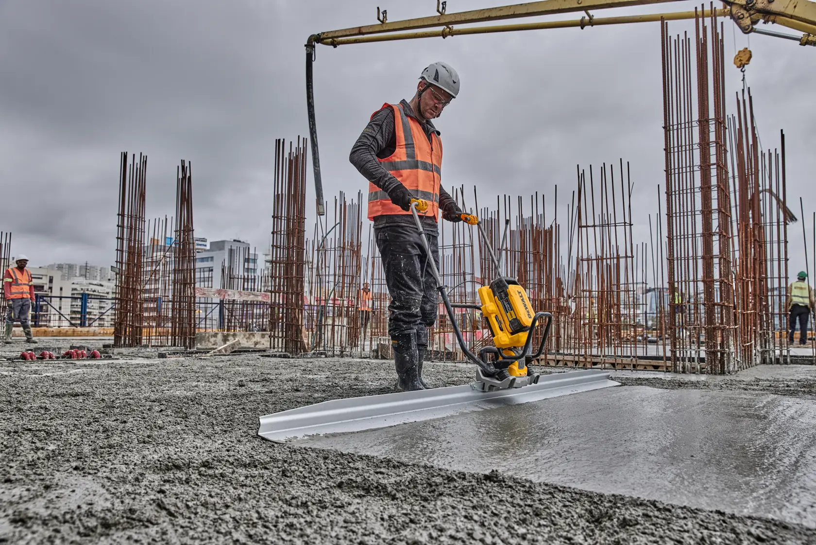 Worker uses a DEWALT power tool to smooth concrete at a construction site; steel rods are visible in the background.